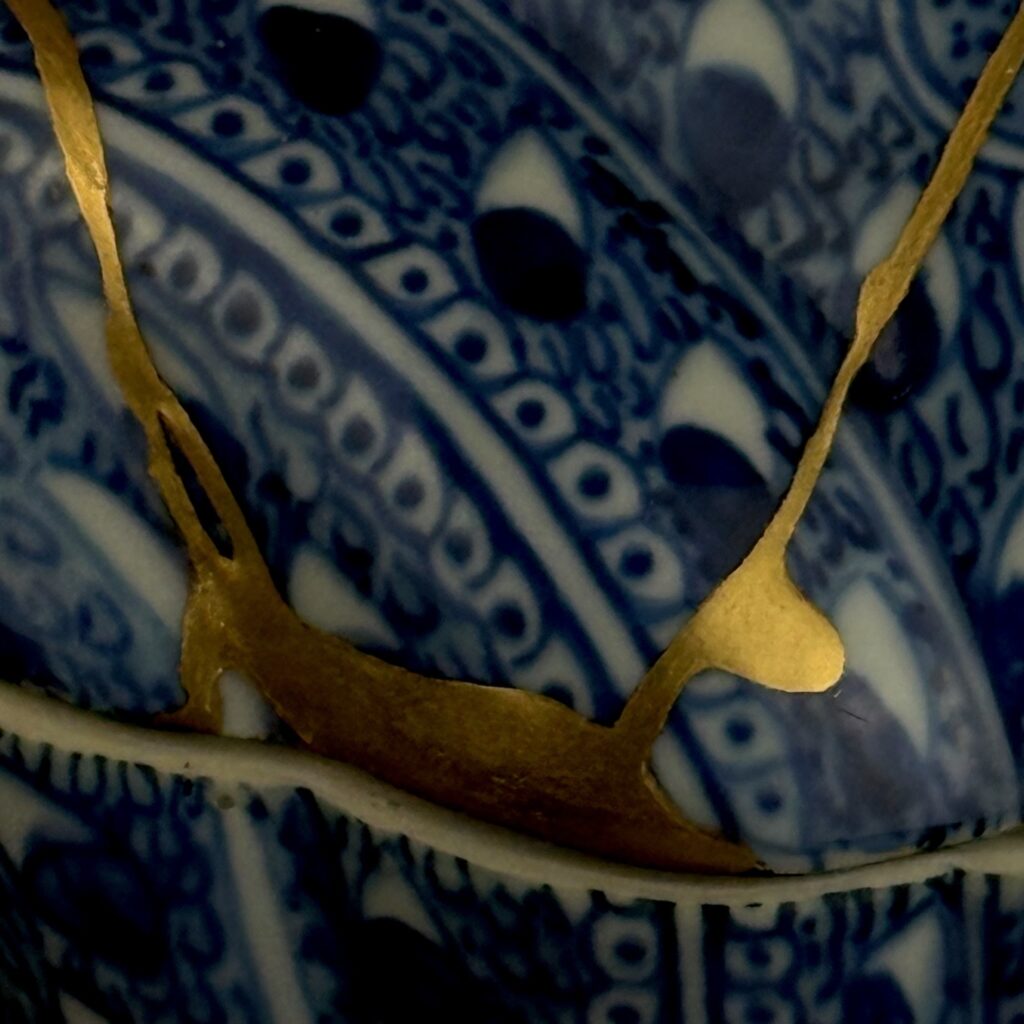 Nahaufnahme einer breiten Goldnaht, die auf die Deckelkante trifft, umgeben von blauem Rankenmuster