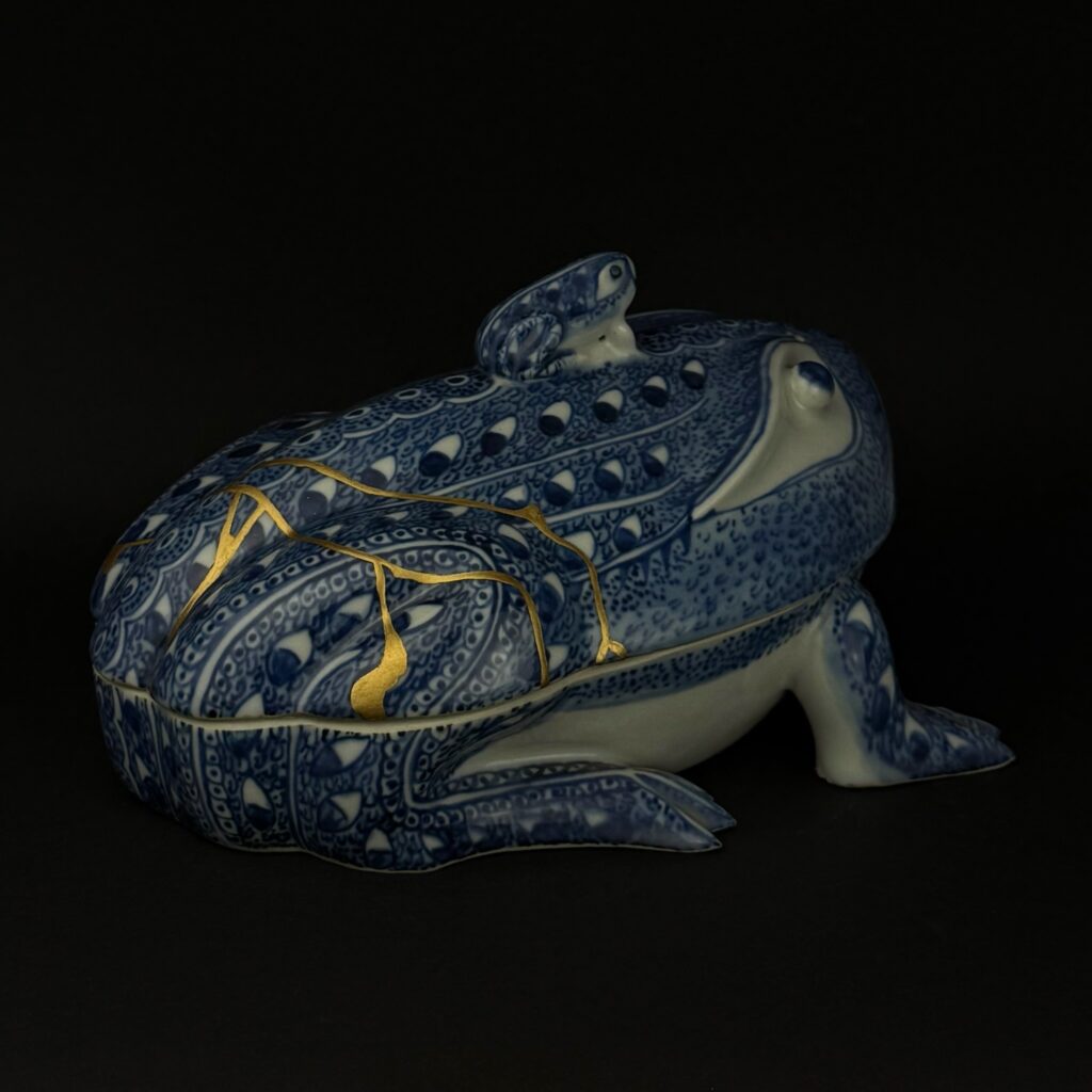 Alt: Rückansicht der Porzellandose mit verzweigten Goldnähten und kleinem Frosch auf dem Deckel