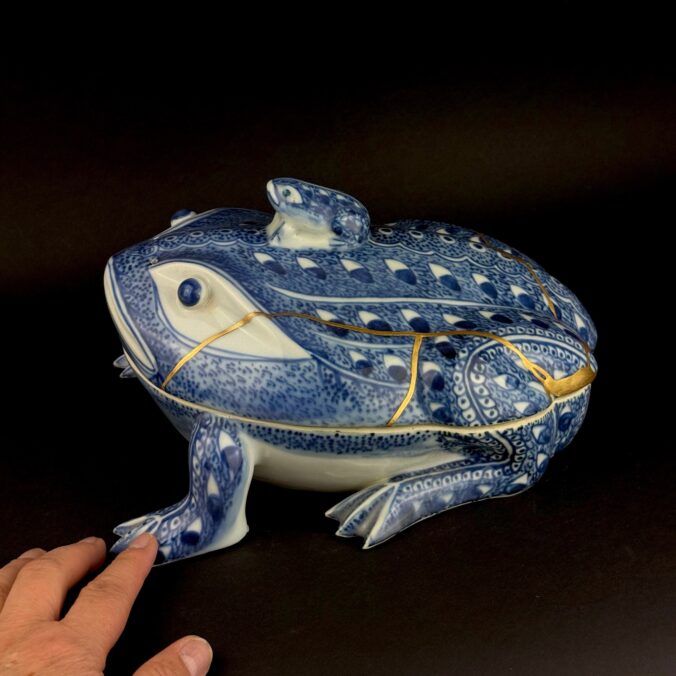 Porzellanfrosch mit kleinem Frosch als Deckelknauf, davor eine Hand, die die Größe zeigt