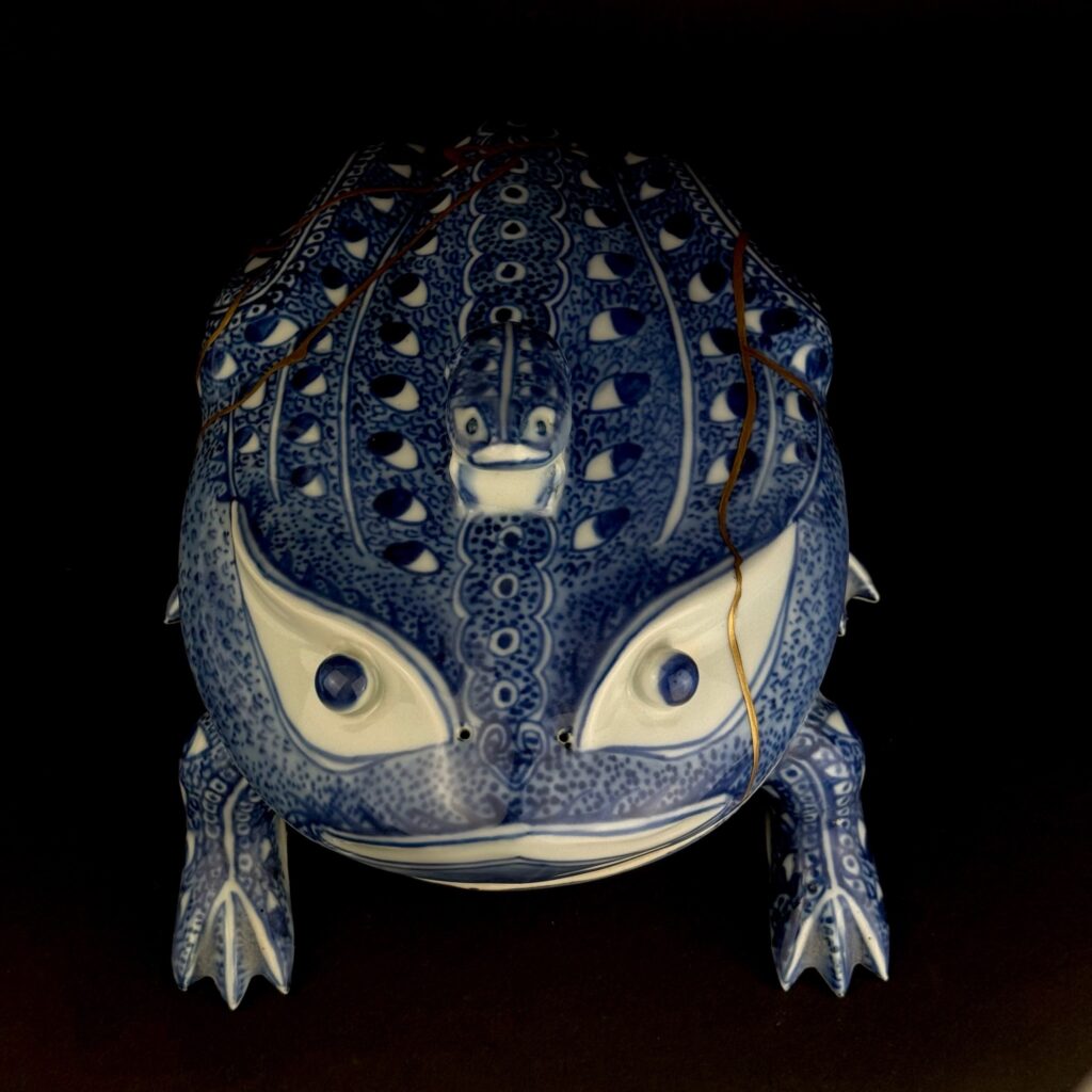 Alt: Frontale Ansicht des Frosches mit hellen Augenpartien, Knauffrosch und feinen Gold- und Lacklinien auf dem Deckel